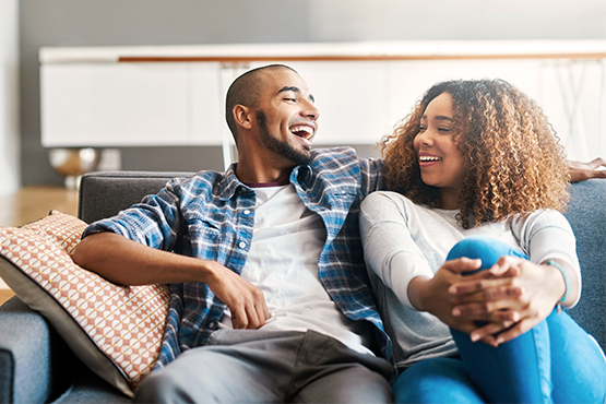 two relaxed and smiling first time home buyers, kicking back together on a blue sofa