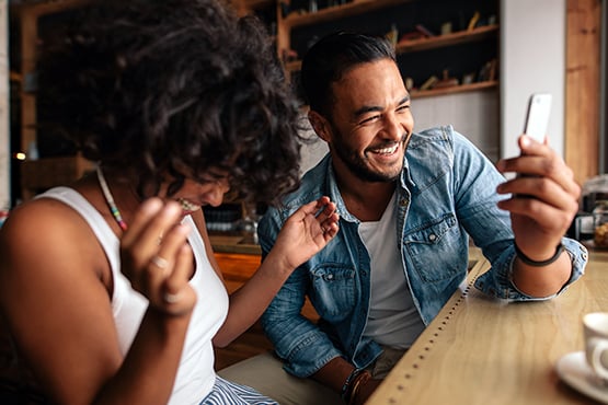 happy man and woman sit at table with smartphone and enjoy information security