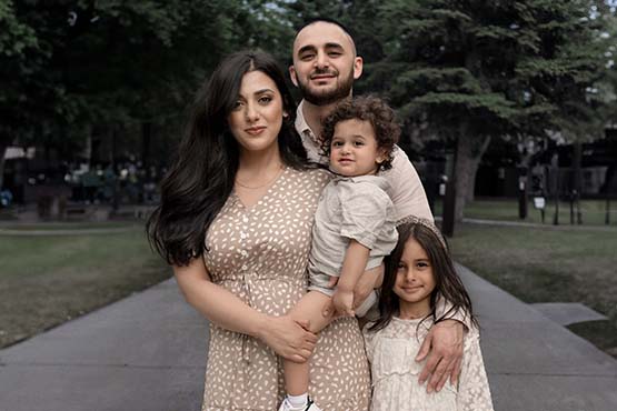 Lezan Tahir, his wife Izzy and their two young children smile for the camera while walking on a sidewalk on a beautiful day