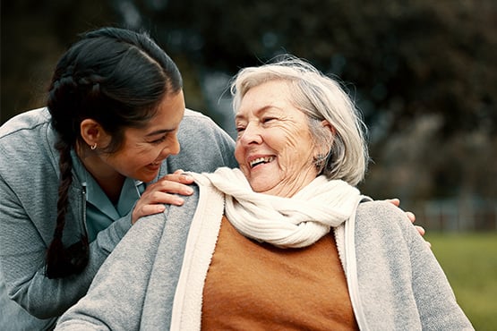 A young woman and a female senior citizen share smiles outdoors after learning tips to fight elder financial abuse