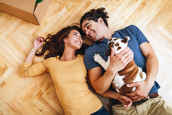 couple falls on floor and smiles at each other while man holds English bulldog puppy