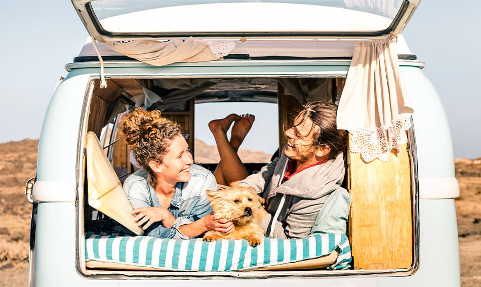 happy young couple and dog lay back and relax in back of vintage RV on a sunny day