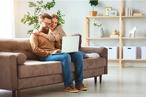 happy young couple sits on couch with computer and enjoys financial education