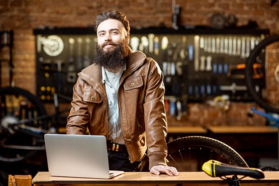 confident burly bicycle repairman uses laptop in shop to enjoy simply business checking