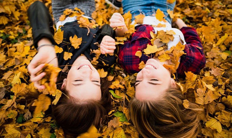 Two teen girls, upside down and giggling in a pile of autumn leaves in their backyard in Bismarck, ND