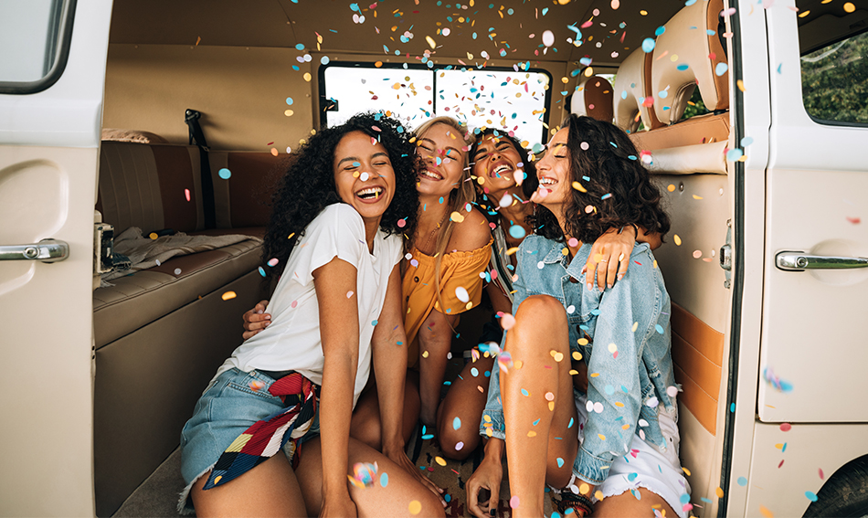 Four happy female friends surrounded by confetti huddle together 