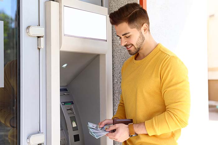 happy man in yellow shirt obtains cash with no fees from the nearest ATM