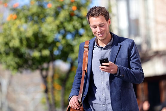happy professional young man walks while looking at phone