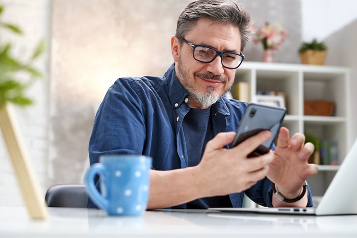 man with glasses and blue shirt uses phone to check Gate City Bank interest rates