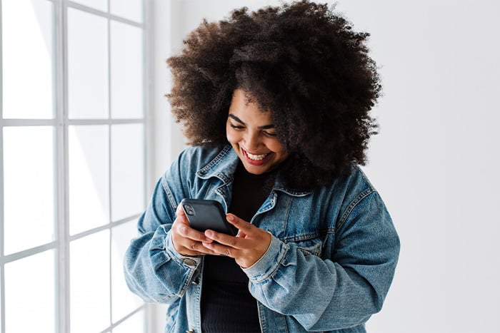happy woman in jean jacket holds smartphone in bright room while using text banking