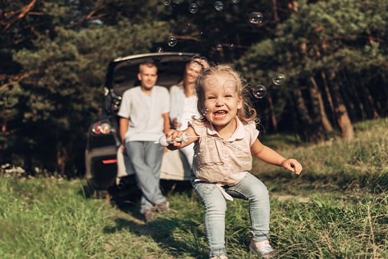 a toddler blows bubbles with her parents in the woods of Minnesota while on a road trip adventure in their family car