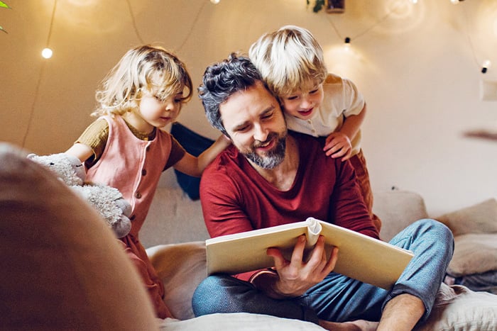 happy dad sits down to read to young daughter and son