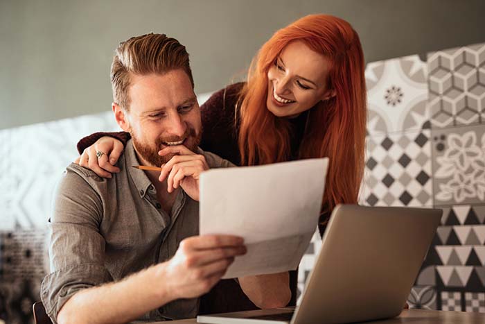 happy young couple smiles and looks at financial plans at a table