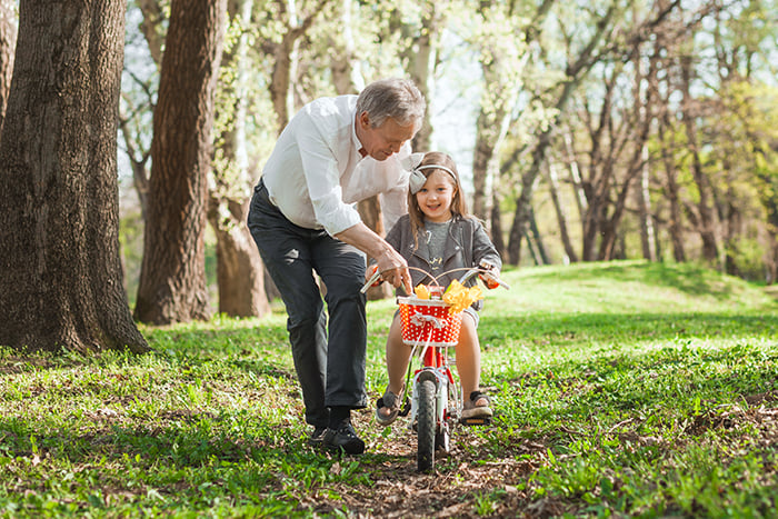 joyful grandfather and granddaughter practice riding a bike in a sunny field