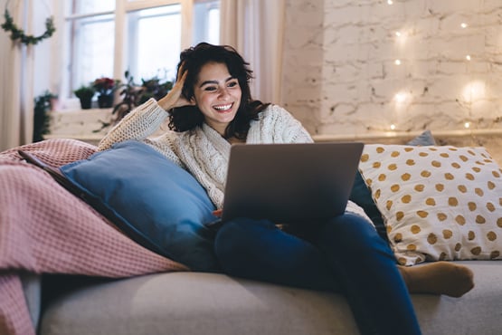 Young woman on a cozy beige sofa, looking at homes for sale on her laptop in Fargo, ND