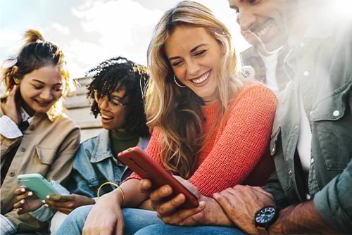 Group of young friends sitting on bleachers in sunny Fargo, ND, opening new Gate City Bank checking accounts via mobile 