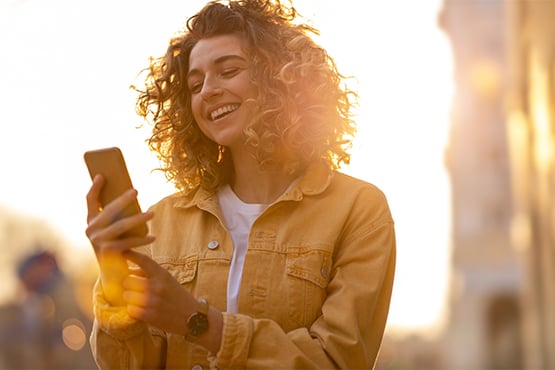 happy woman uses mobile banking on smartphone with a bright sunset in background
