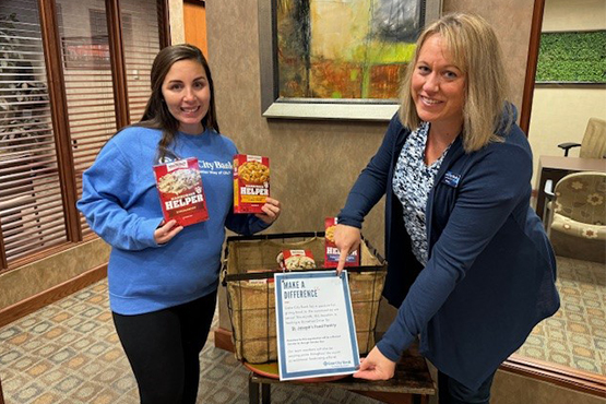 Two female Gate City Bank team members smile and pose for a picture in front of a food-drive box