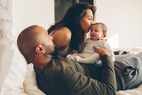 mom kissing newborn baby on the forehead, snuggled beside her husband in their new home