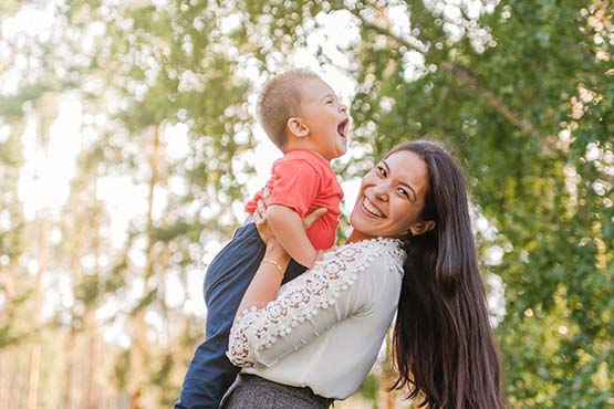 Young woman holding up her laughing son on a sunny day in Wahpeton, North Dakota