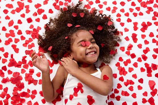 Giggling girl surrounded by red heart-shaped confetti, celebrating Giving Hearts Day in Fargo, ND