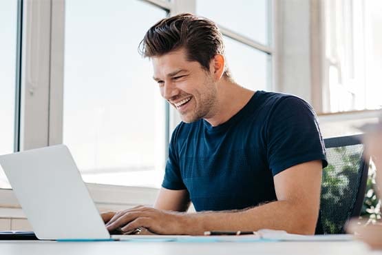 smiling young man in a navy shirt, scrolling through free financial education resources on his laptop