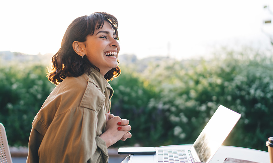happy woman sits at patio table with laptop and scenic backdrop to read Gate City Bank’s article on keeping deposits secure with FDIC insurance