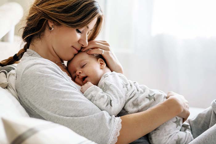 Young woman sweetly cradling her sleeping baby on her chest, relaxing in their new home in Fargo, ND