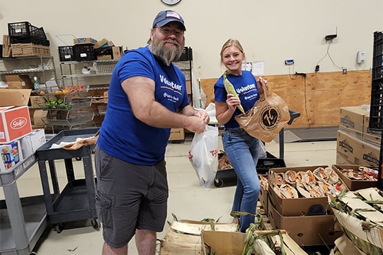 Man and woman who work for Gate City Bank smile for the camera while volunteering at community food pantry and wearing matching blue t-shirts