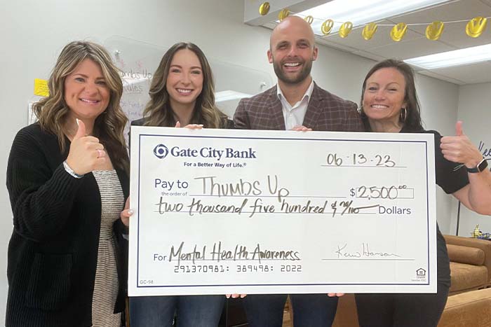 four happy people hold a big check for $2,500 from Gate City Bank to Thumbs Up in Elk River, MN