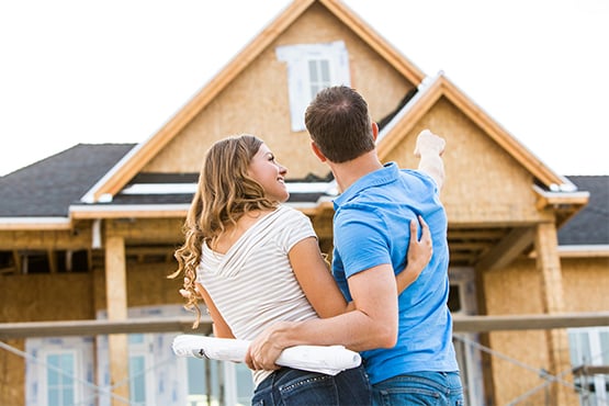 wife smiles up at her husband as they tour the building lot for their new home and look at the roof under construction