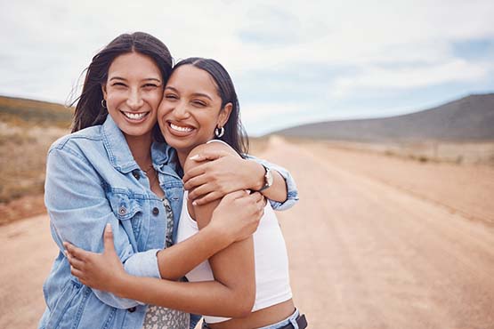 Two young woman on a gravel road under blue skies, posing for a photo together on the edge of Williston, ND