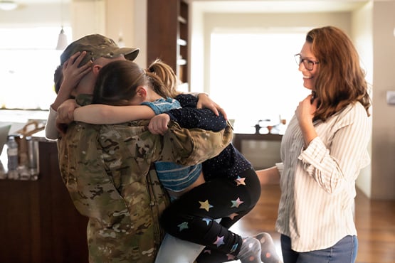 Military dad hugs children in their new home purchased with a VA loan from Gate City Bank