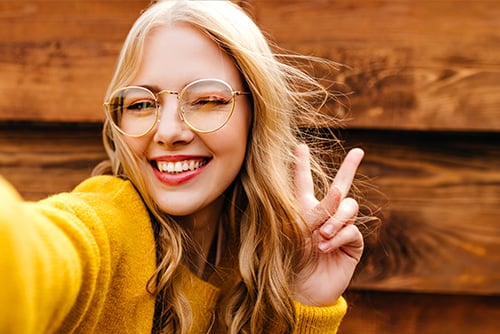 Smiling blonde woman in a gold sweater, making a peace sign on her way to open a new checking account in Alexandria, MN