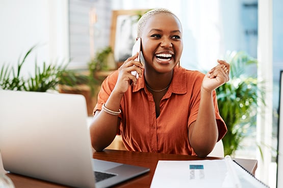 A joyful female business owner talks on the phone after learning key tips about the self-employment tax from Gate City Bank