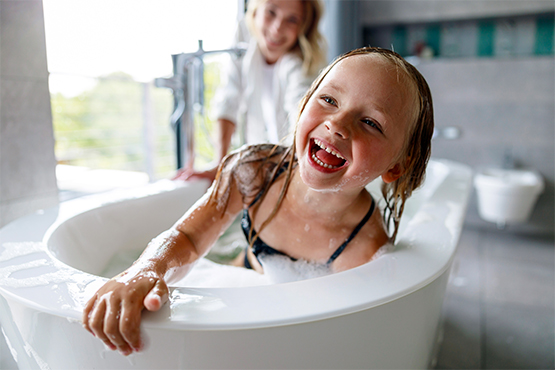 giggling blonde girl taking a bubble bath in a soaker tub in her family's newly remodeled master bathroom