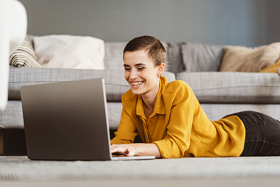 A smiling woman works on her laptop on her apartment floor while staying protected from tax scams with Gate City Bank