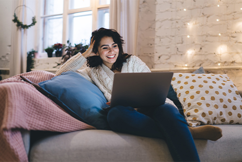 Young woman on a cozy beige sofa, looking at homes for sale on her laptop in Fargo, ND