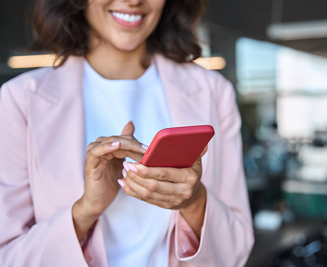 Closeup of brunette woman in a pale pink blazer, making her business loan payment on her Gate City Bank mobile app