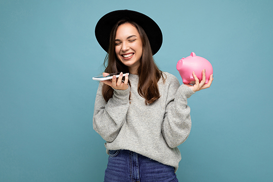 smiling woman holds a piggy bank and cell phone after reading tips on handling unexpected money