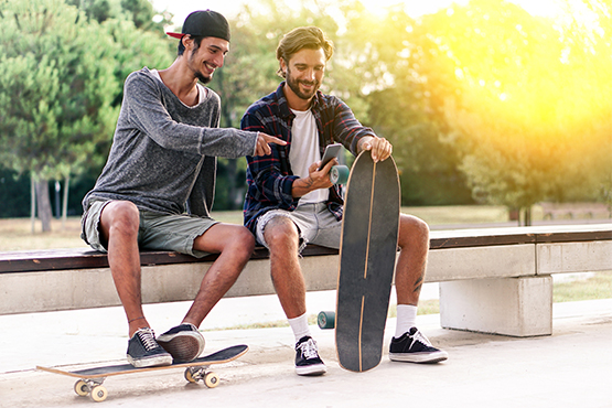 two happy male skateboarders sit on bench and enjoy debit card rewards on phone