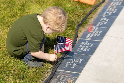 young boy plants small American flags next to memorial bricks at Veterans Memorial Park in Grand Forks, ND