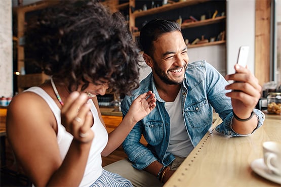 happy man and woman sit at table with smartphone and enjoy information security