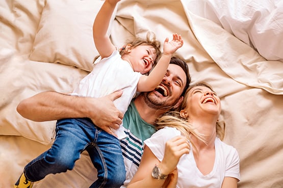 mother father and young child laugh as they fall back after a fun pillow fight