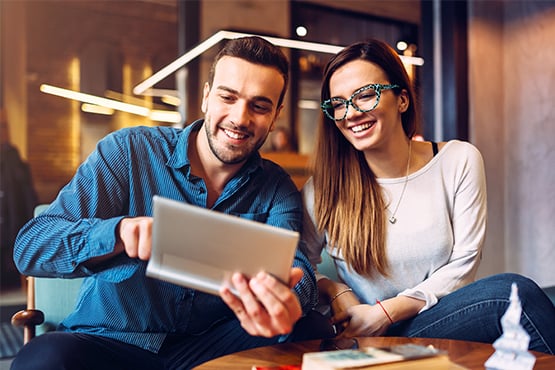 Happy Gen Z woman in tortoiseshell glasses, looking at a tablet and opening a free checking account with her boyfriend