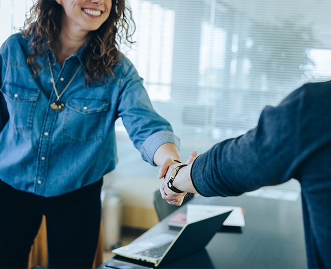 Happy young woman in denim shirt shaking hands with her Gate City Bank personal lender in Fargo, ND 