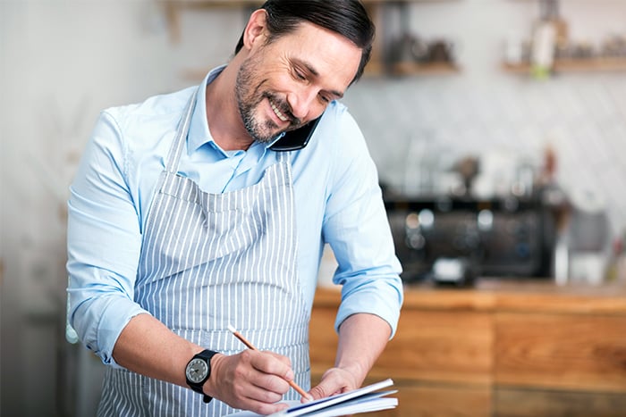 happy man takes notes and enjoys business services while talking on phone