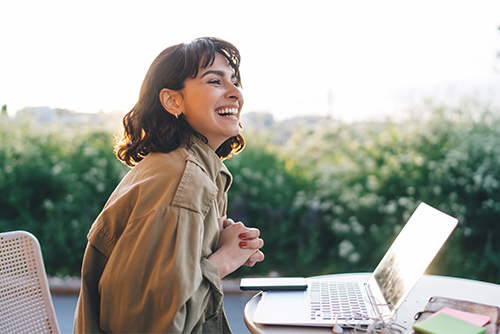 happy woman sits outdoors with laptop on a sunny day while enjoying peace of mind with FDIC coverage