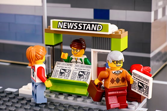 three lego people swap newspapers at news stand attributed to gate city bank's news coverage