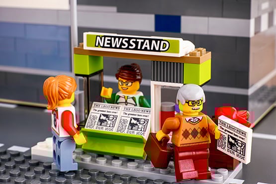 three lego people swap newspapers at news stand attributed to gate city bank's news coverage